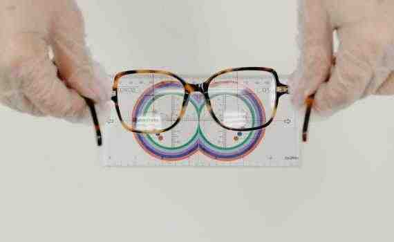 From above of crop anonymous oculist in sterile gloves measuring modern eyewear with optical tool on white background