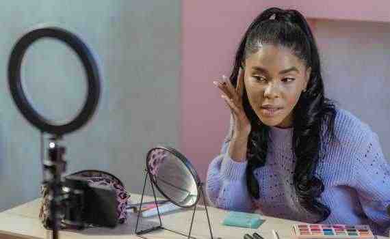 Focused black blogger applying makeup and recording video