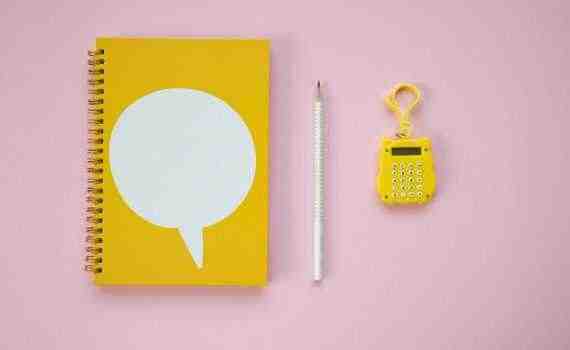 A Yellow Spiral Notebook and Calculator on a Pink Surface