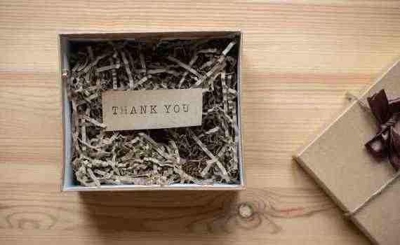 Top view of opened carton present box with small postcard with Thank You inscription and paper stuffing on wooden table