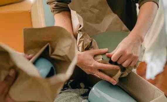 Crop unrecognizable person packing ceramic tableware in parchment