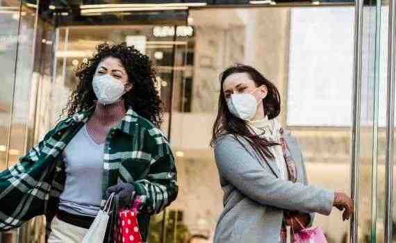 Low angle of woman with purchases in colorful shopping bags walking through doors of store during coronavirus pandemic