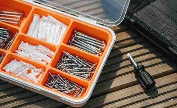 From above of container with assorted instruments placed on wooden surface near screwdriver and black case on street in sunlight