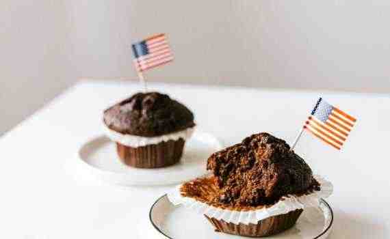 From above of bitten and whole festive chocolate cupcakes decorated with miniature american flags and placed on white table